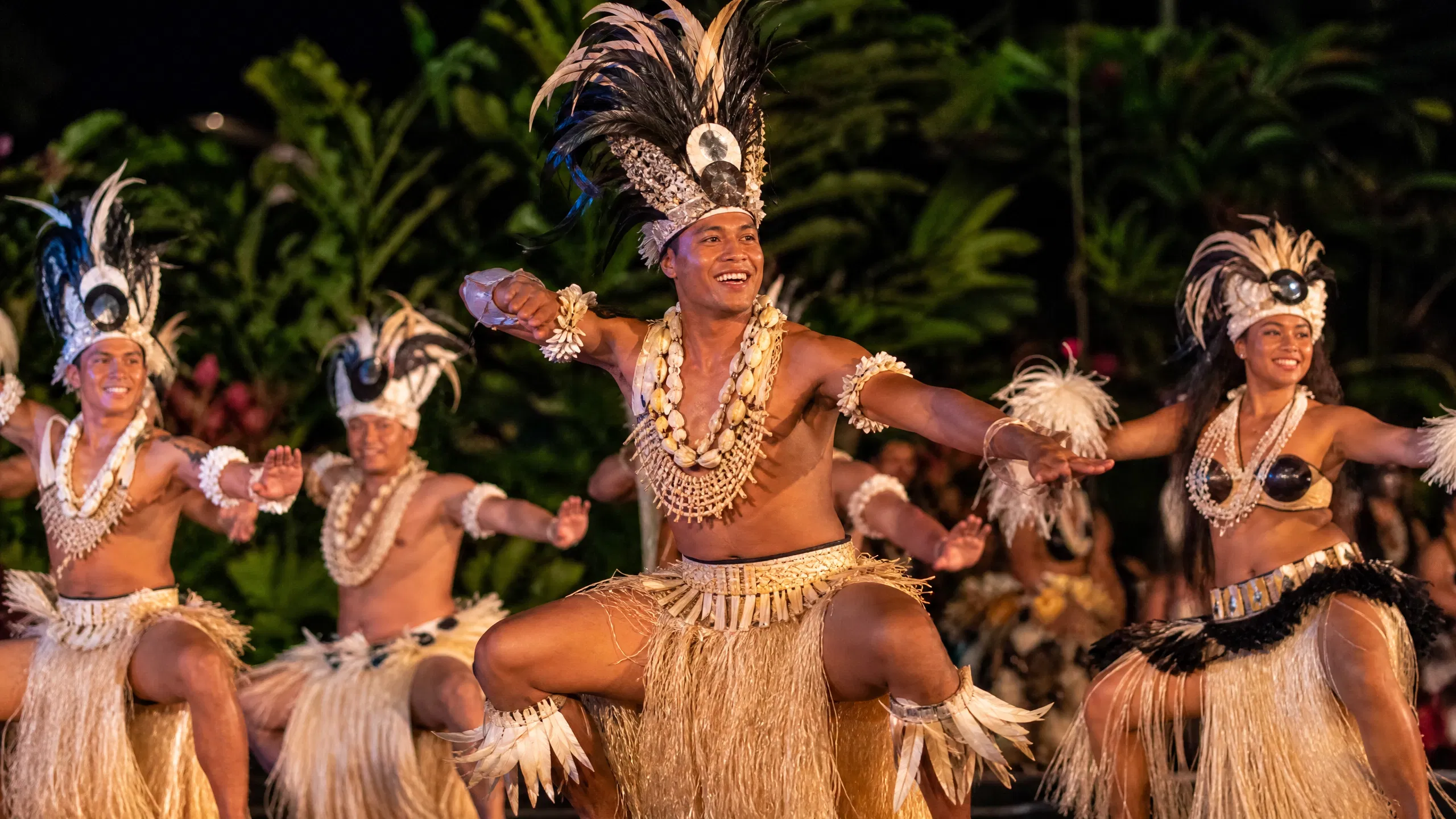 E4wF3Y4qIuJwVadeIhwe5H 1787103203799 na1fn L2hvbWUvdWJ1bnA professional editorial photograph of traditional Cook Islands dancers in intricate Polynesian costumes made of fibers and shells, performing an energetic rhythmic dance on a stage under warm evening lighting.