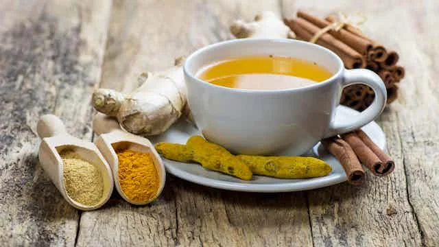 Alt Text: A professional editorial photograph of cinnamon sticks, turmeric powder, and fresh ginger root on a clean kitchen counter next to several prescription pill bottles, symbolizing the intersection of natural ingredients and modern medicine.