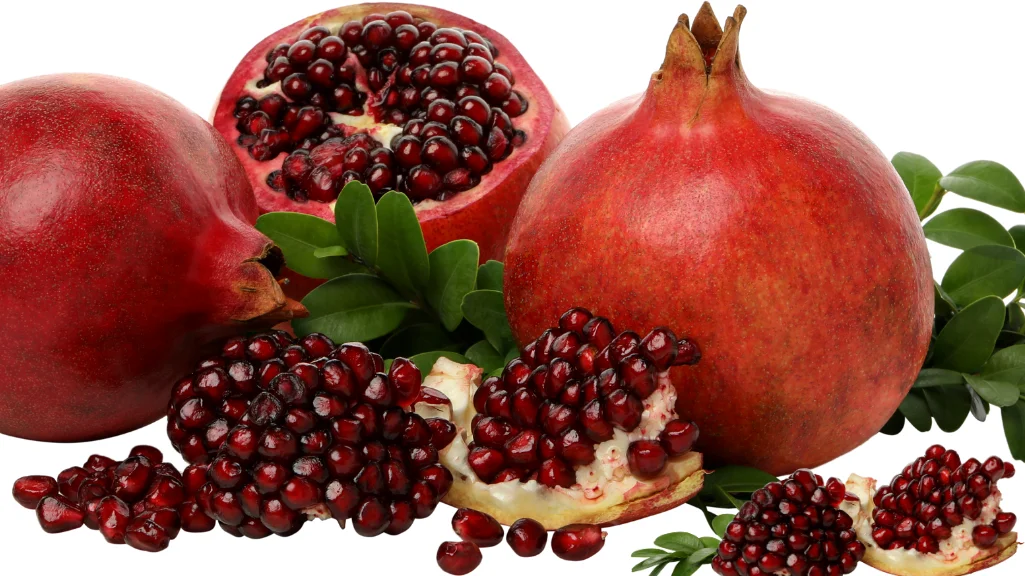 A halved pomegranate surrounded by ruby-red arils on a wooden surface